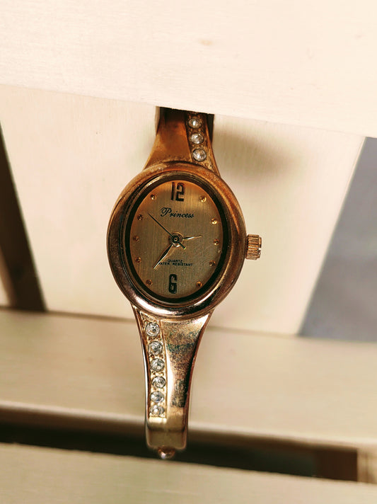 Princess brand pre-owned Quartz bracelet gold tone watch.. champagne color dial .. imitation diamonds along the sibes of bracelet.. casual dress watch
